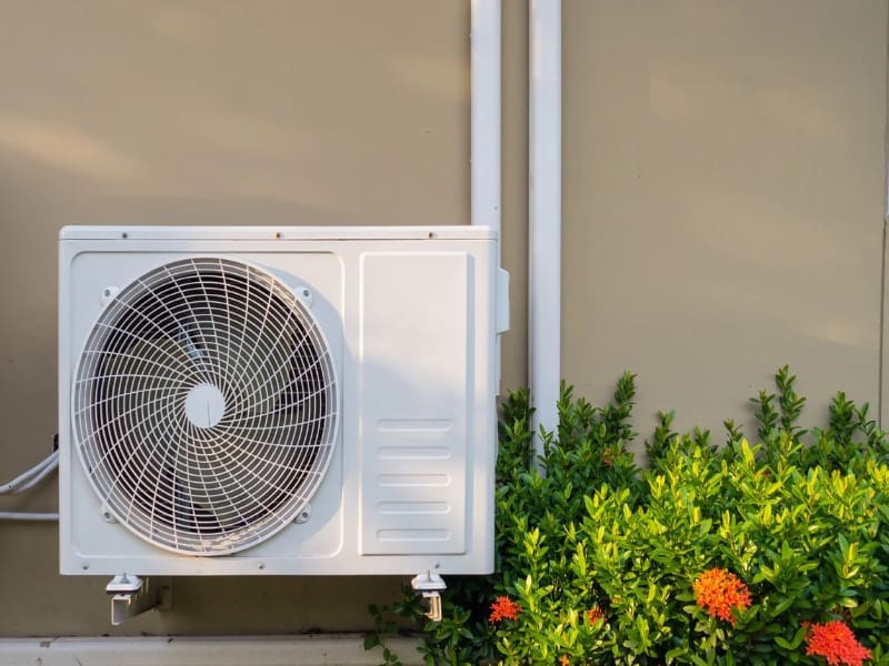 A white air conditioner sitting outside next to some bushes.